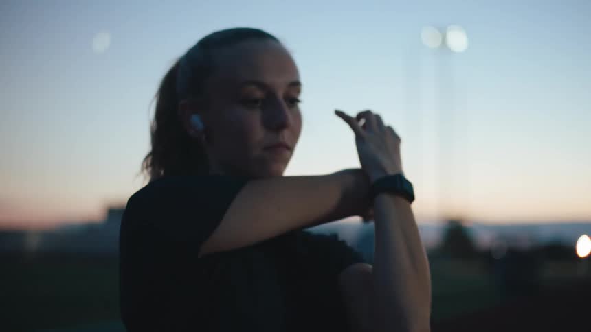 A woman performs stretches near a running track