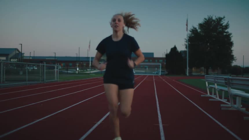 Female athlete runs along running track near audience stands