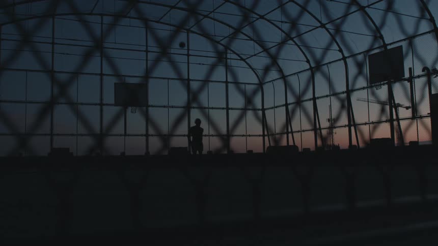 Man silhouetted against the sky at night plays basketball