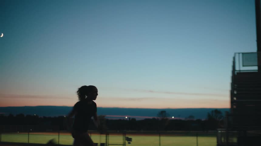 Silhouette of a woman running up outdoors bleachers in the track at sunset