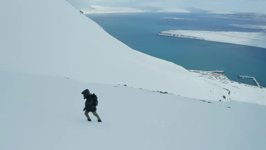 Person climbing a mountain covered in snow with the blue sea in the background