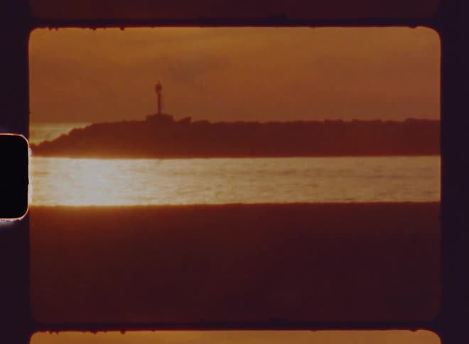 A light house standing on an island is silhouetted against the shining sun