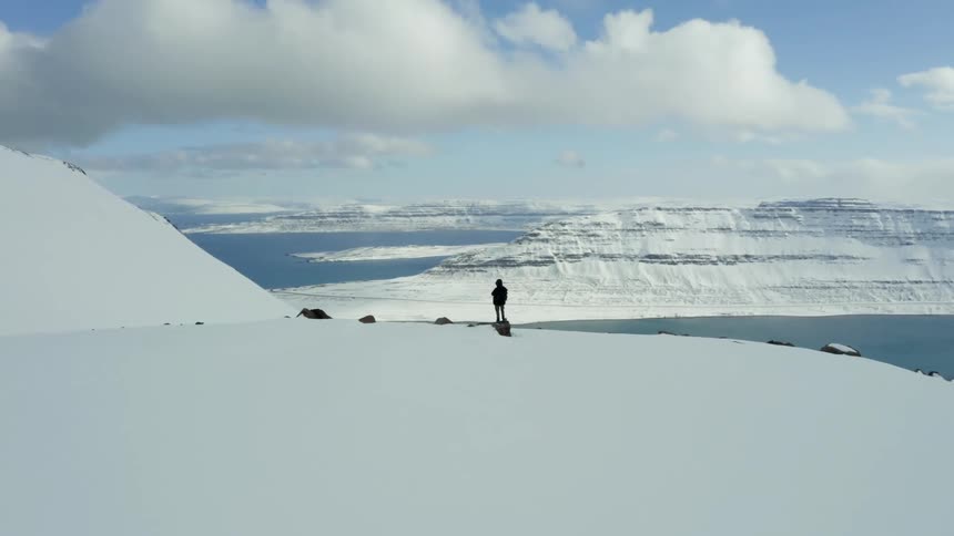 Aerial panorama of a person on a snowcovered mountain peak overlooking the sea