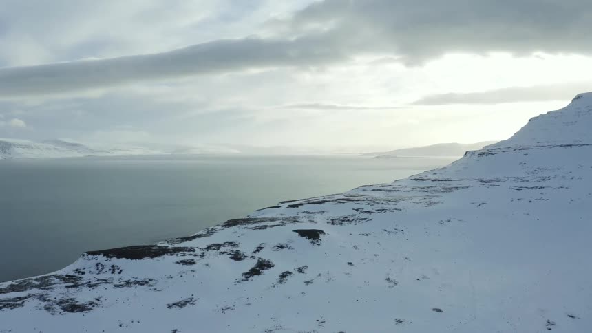 A mountainous snowy landscape near the ocean at sunset