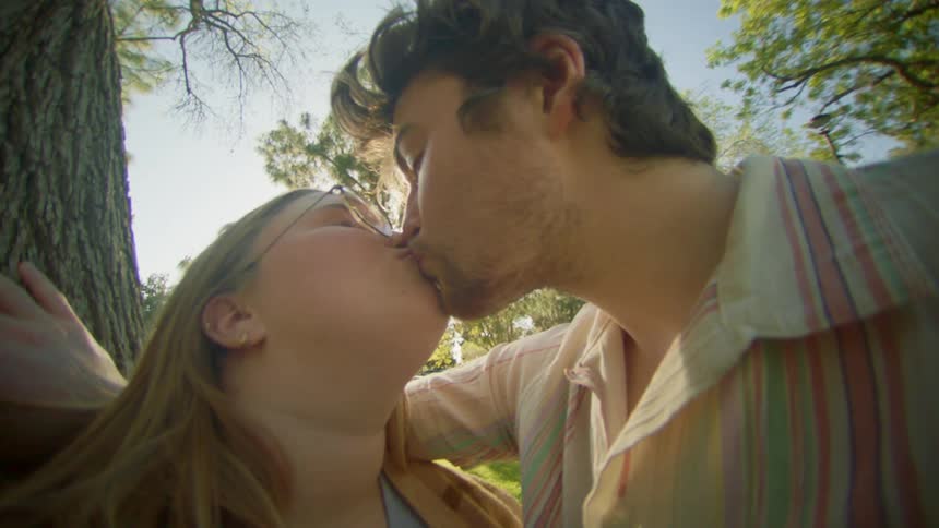 A man and a woman kiss under a tree