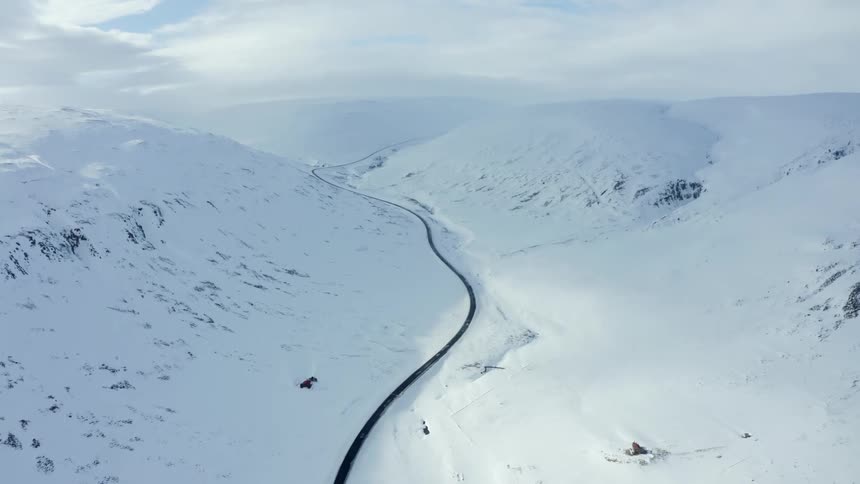 Aerial view of a car driving down a road in a snowy valley