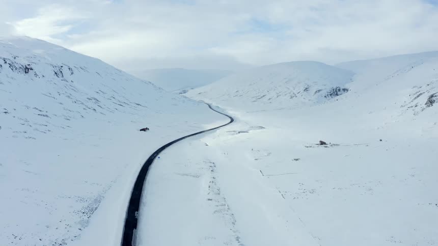 Aerial panorama of a winding and narrow road in the middle of snowcovered mountains