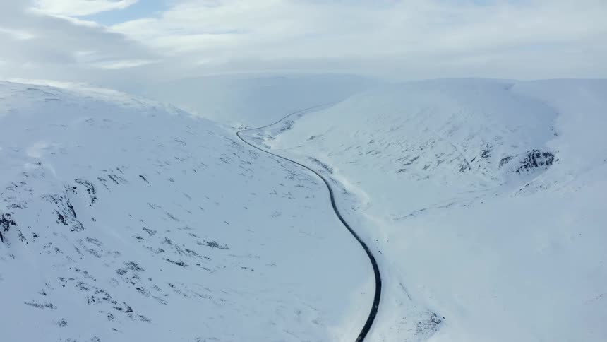 A long empty road runs through the snow covered mountains