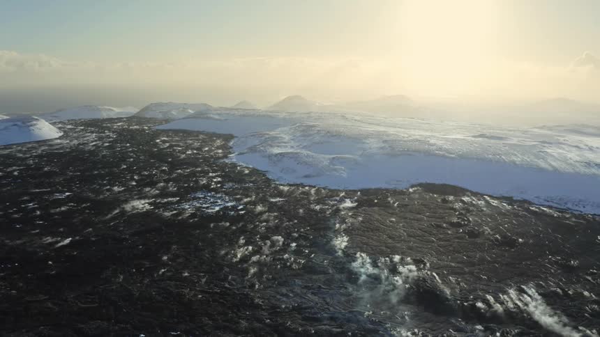 Aerial panorama of a peninsula with a blue sea and snowy mountains with the sun on the horizon