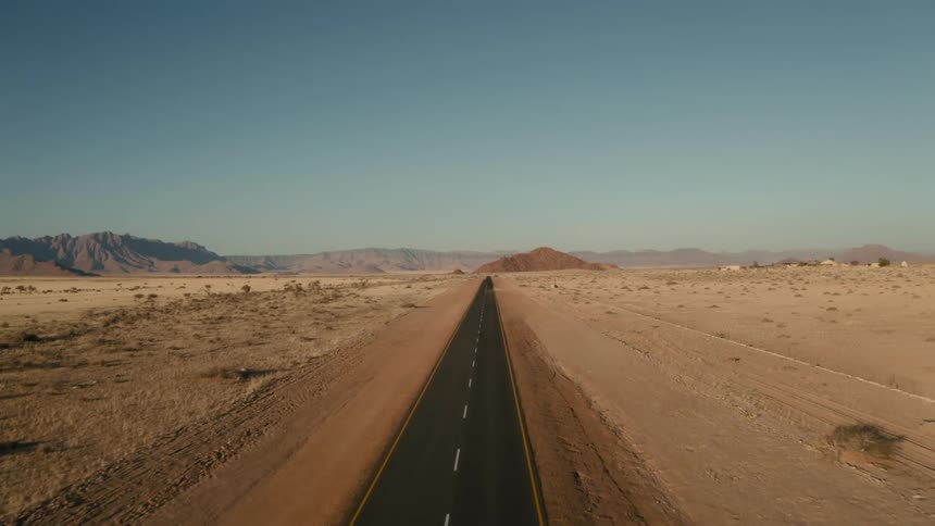 A large asphalt road in a desert with mountains in the background