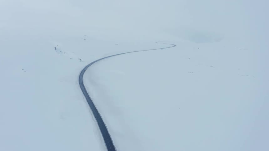 Aerial view of a long winding road in the middle of snowy mountains