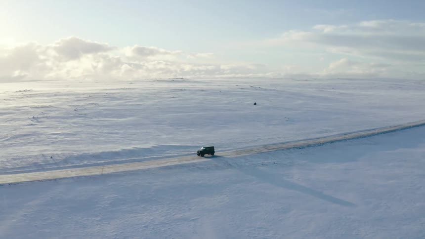 Black jeep traveling on a road surrounded by a natural environment covered by snow with the morning sun on the horizon