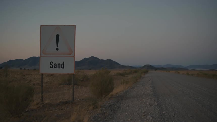 A road sign signalling danger from sand on a desert road