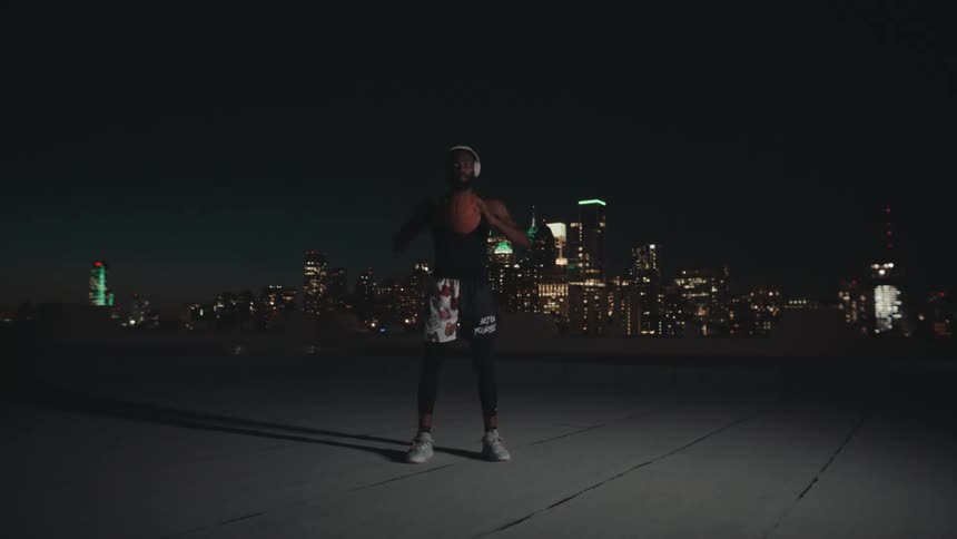 Man with headphones and holding a basketball on the terrace of a building with a panoramic view of a metropolis illuminated at night