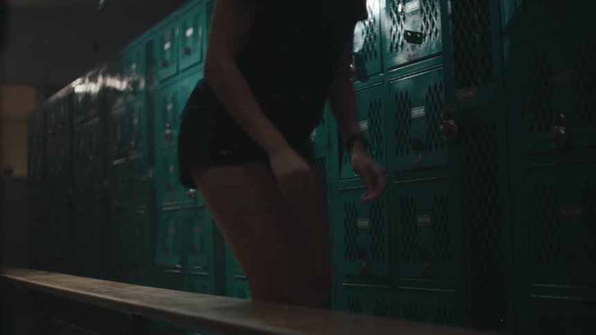 A blonde teenager stands up in a locker room and walks away