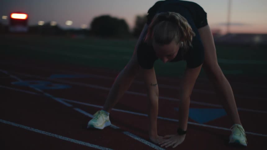 A fit woman wearing sports clothes stretching on a field at sunset