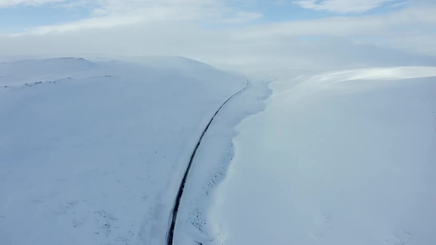 An aerial view of a snowcovered landscape with a single dark winding road cutting through