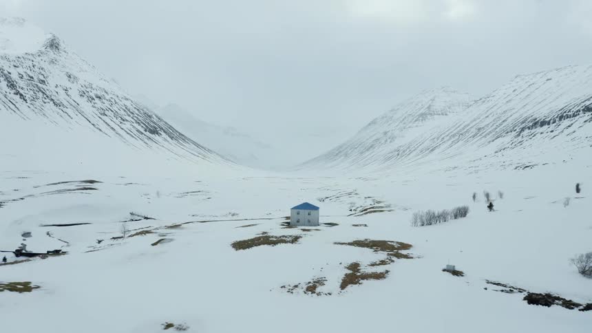 Isolated house on a snowcovered plateau with mountains around on a cloudy day