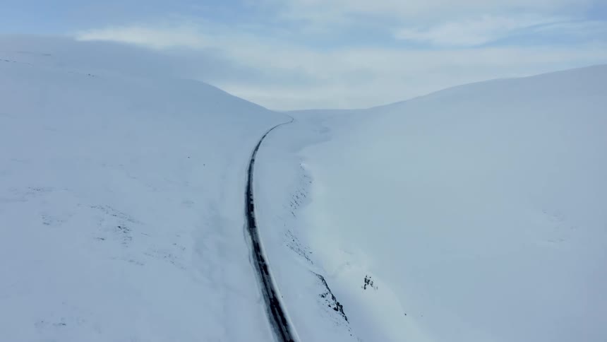 A car travels on a remote highway through a snowcovered mountain range