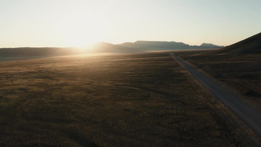 Sun glares over mountains onto fields and an empty highway