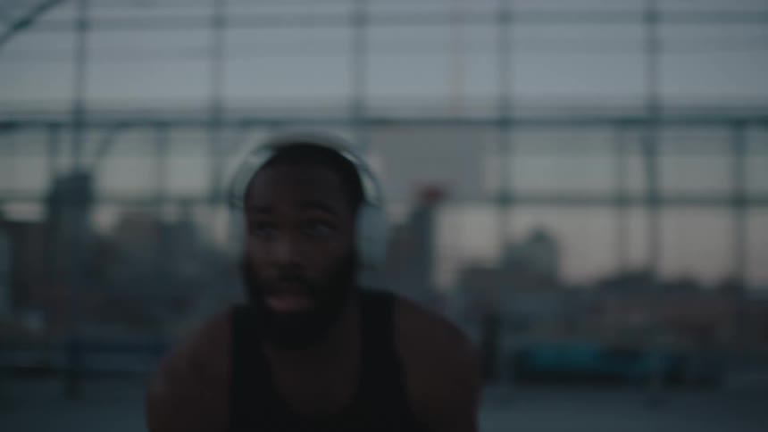A man wearing headphones playing basketball by himself