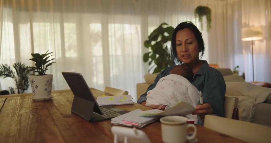 A woman sitting is looking at a paper and has a notebook in front of her on the table