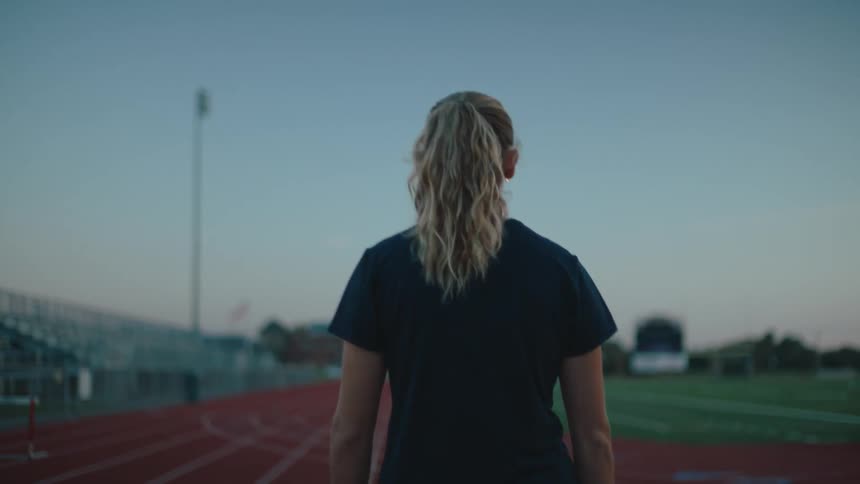 A woman wearing a ponytail and a black tshirt walking on sport tracks