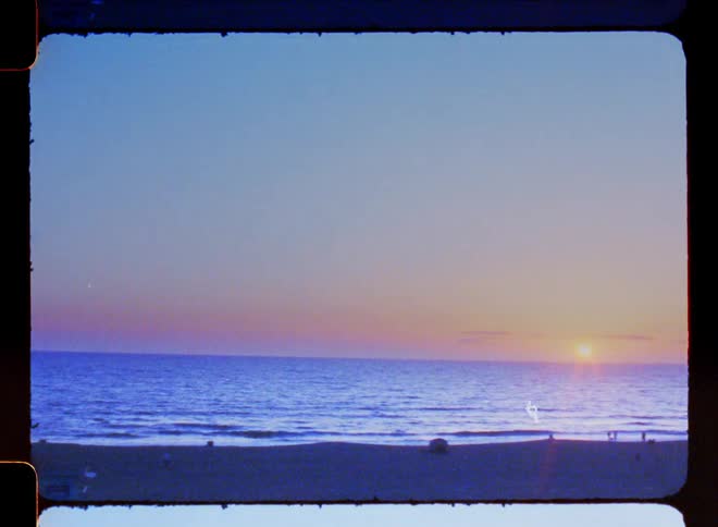 A sunset on a beach with the sea reaching the horizon and the sky with blue and orange colors