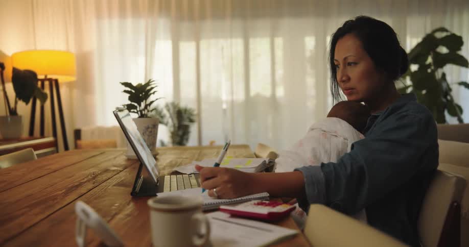 A woman sitting at her table holding her baby while on video call with a male coworker