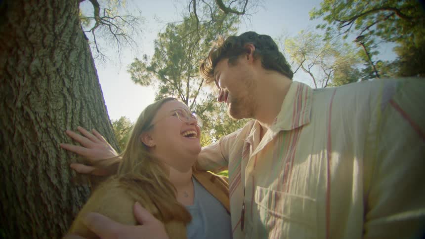 Couple leaning against tree hug and laugh together on a sunny day