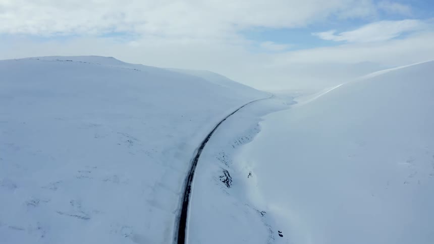 Dark road passes along snowy slope in narrow valley during winter