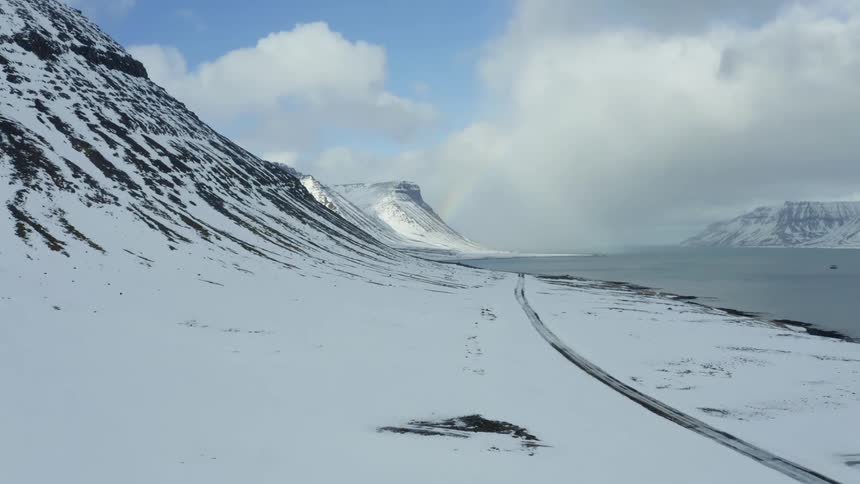 A coastal road between a body of water and a snow covered mountain range