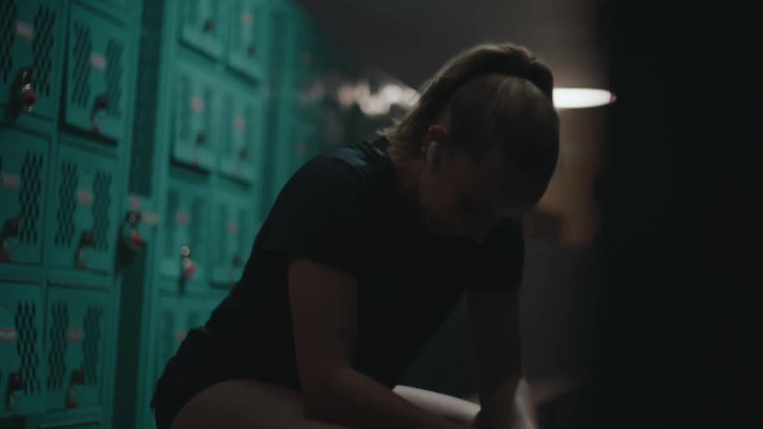 A woman is sitting in the locker room listening to music