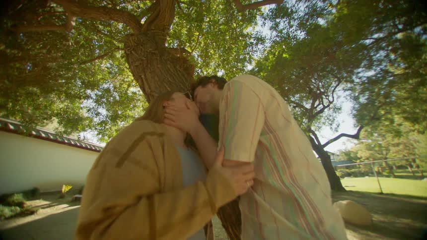 A man and a woman are leaning against a tree and are kissing