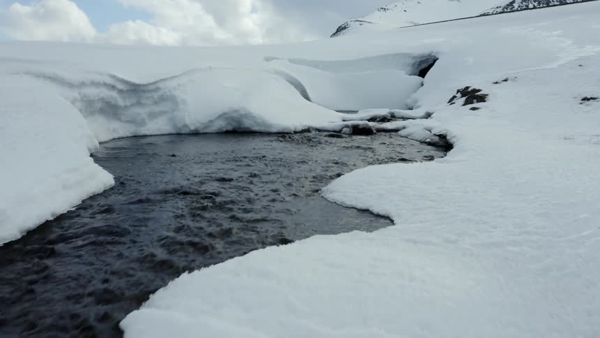 A stream runs from the mountain covered with snow
