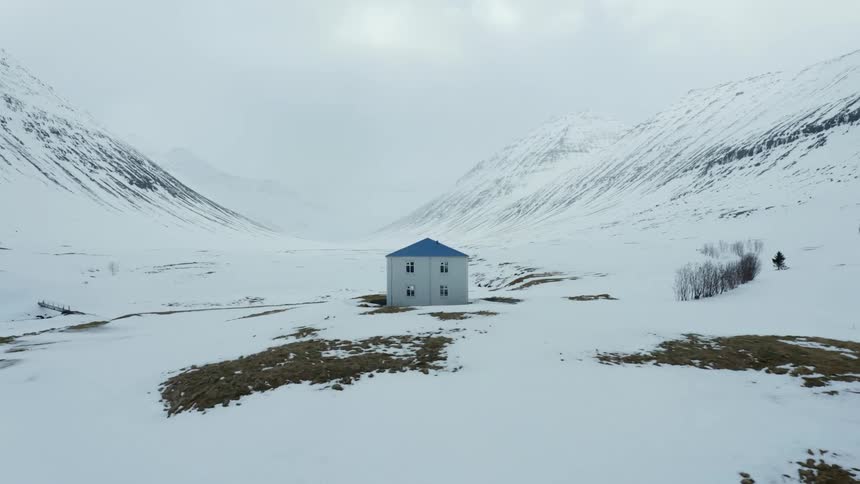 A house with grey walls and blue roof in a region covered by snow