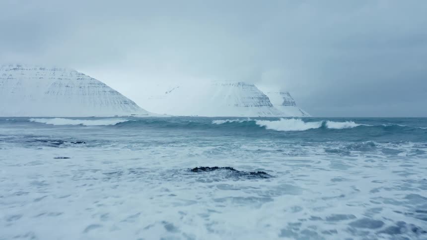 A beach on an arctic sea with two icecovered mountains in the background