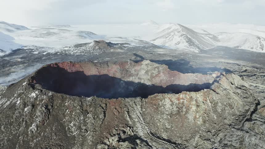 Aerial panorama of a huge crater with mountains around with snow