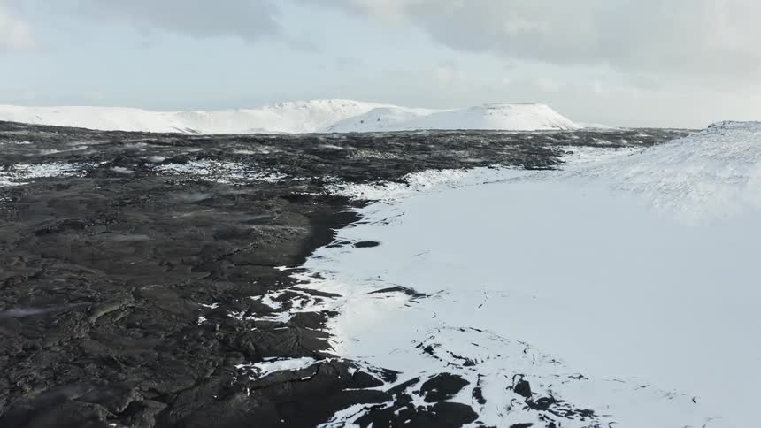 Aerial panorama of a black ground with snowy mountains on a cloudy day