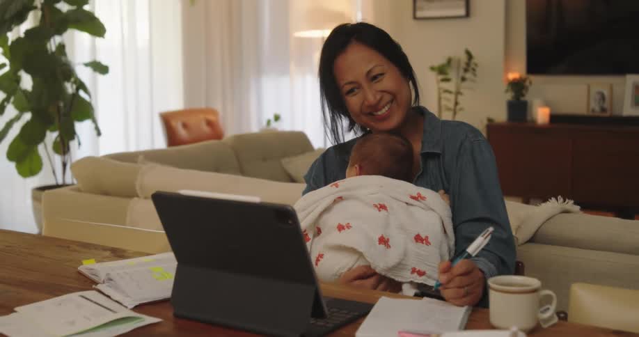 A woman having a cheerful conversation on her laptop while holding her baby daughter in her lap