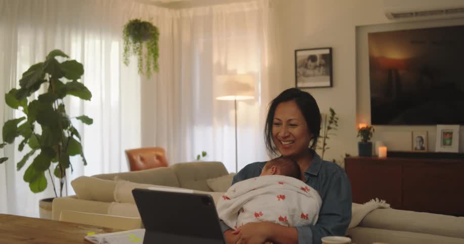 Mother working from home holds baby and smiles during video call