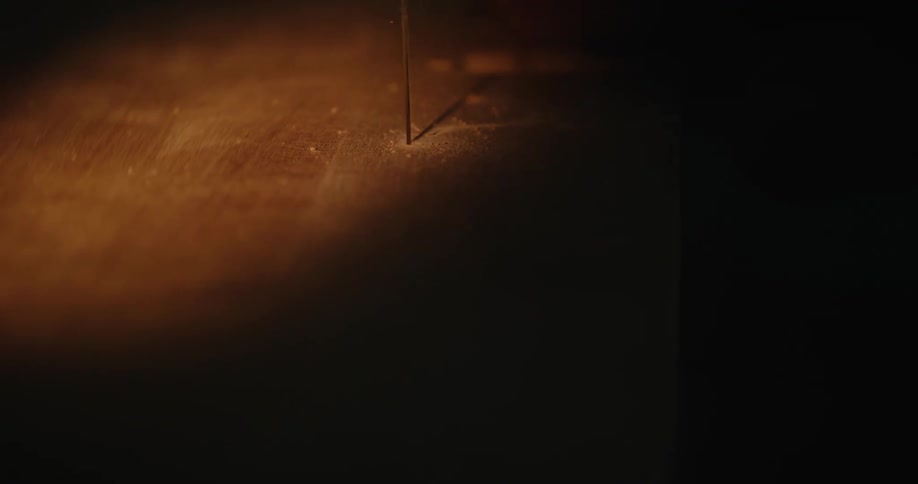 Jigsaw blade saws through thick slab of wood in shadowed area
