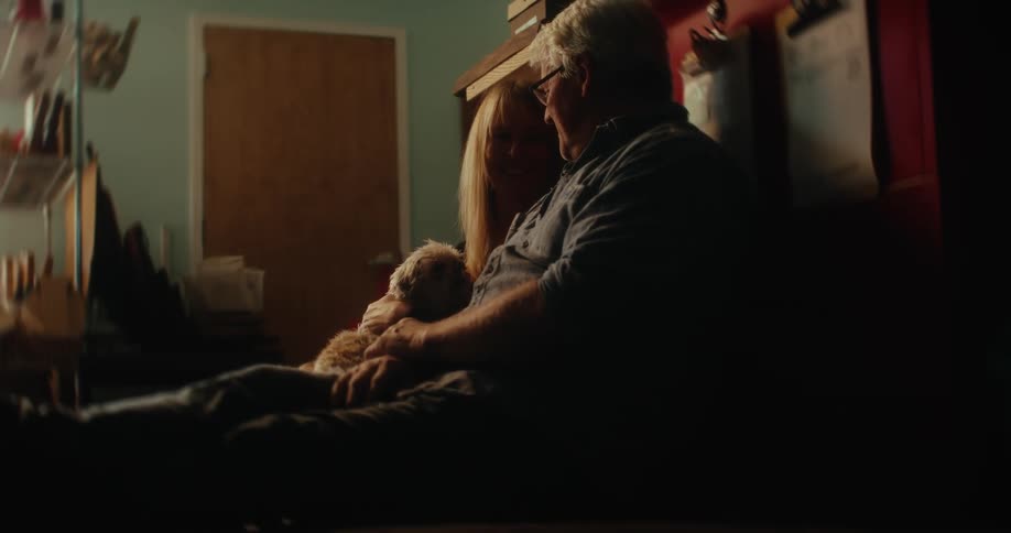 Couple sitting on the floor in a room talking and smiling while the woman holds a dog