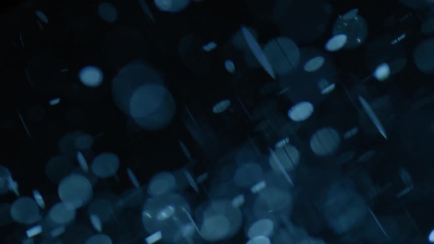Spots of blue tinted light float through darkness