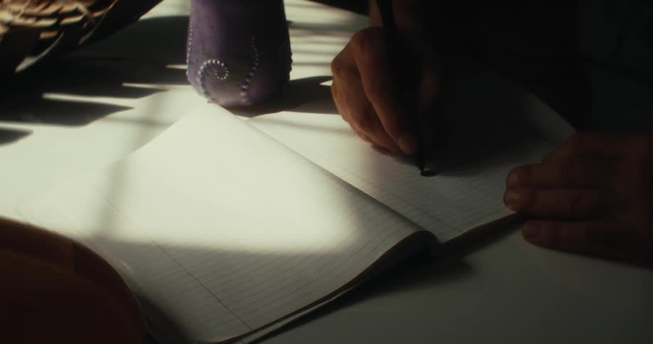 An artist places their drink and sketchbook on a table then begins to draw