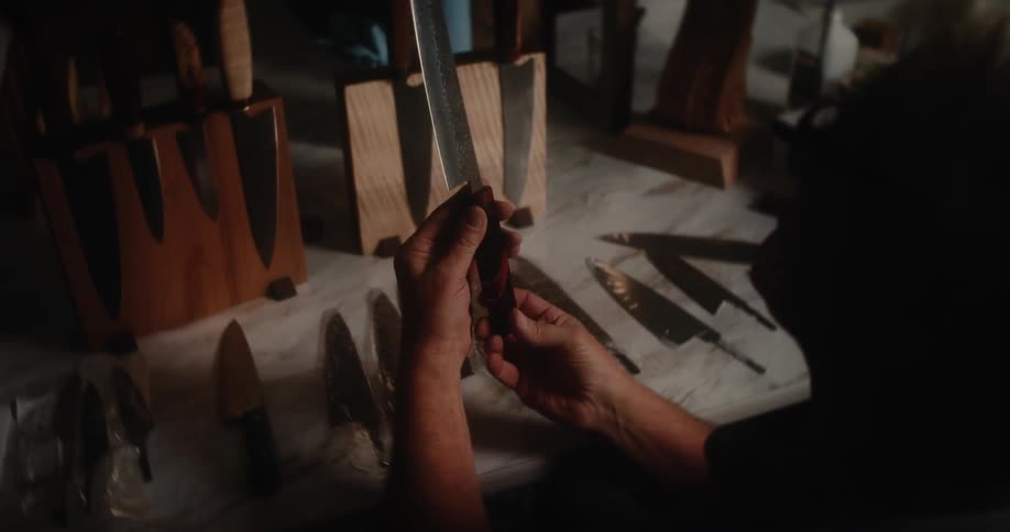 An older male bladesmith inspects finished knives and returns them to their holders