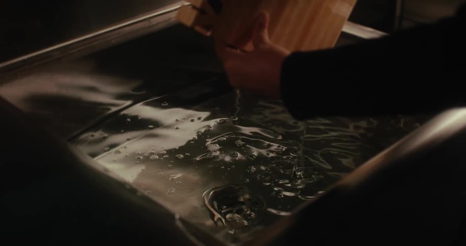 A person lifts a wooden object out of a container filled with liquid