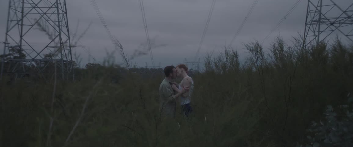 Two people kiss near utility lines