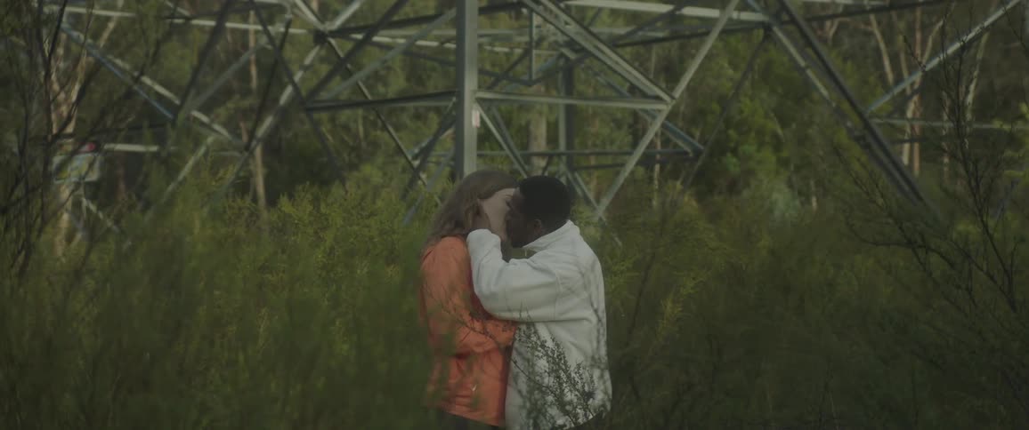 Couple in a wooded location next to a metal tower kissing