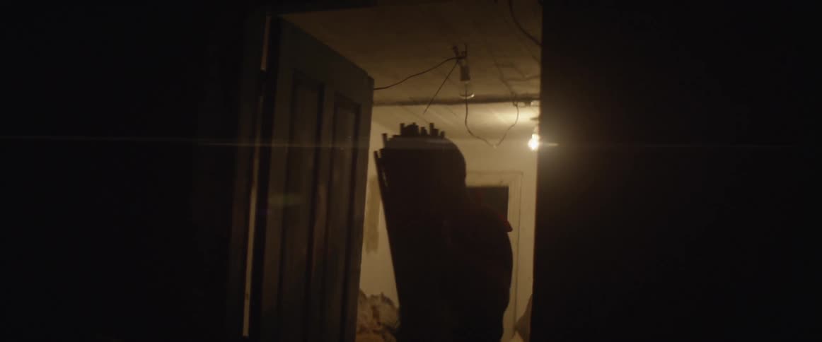 A man carries bundles of sticks through a doorway